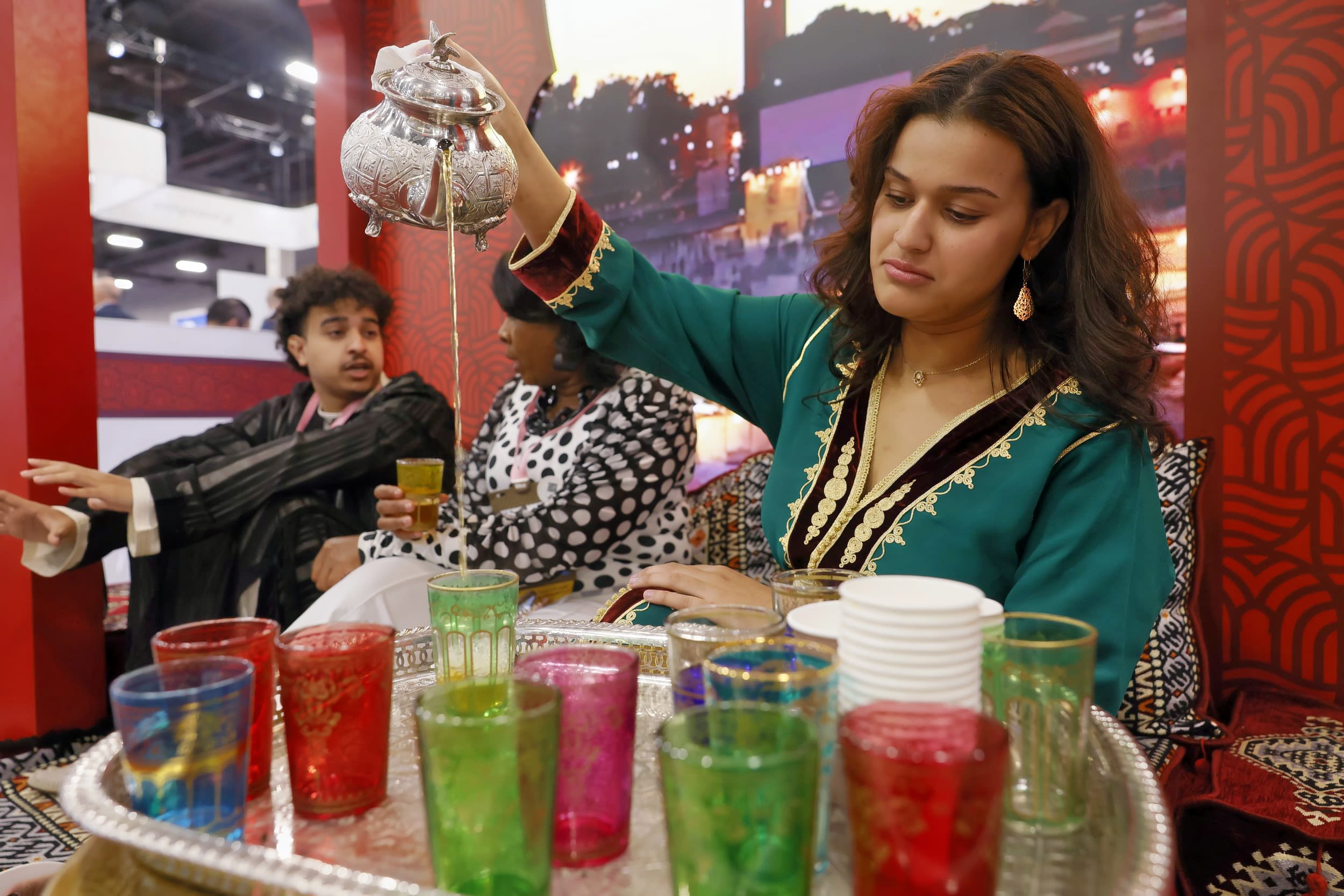 Female in traditional outfit pouring a tea into colored glasses