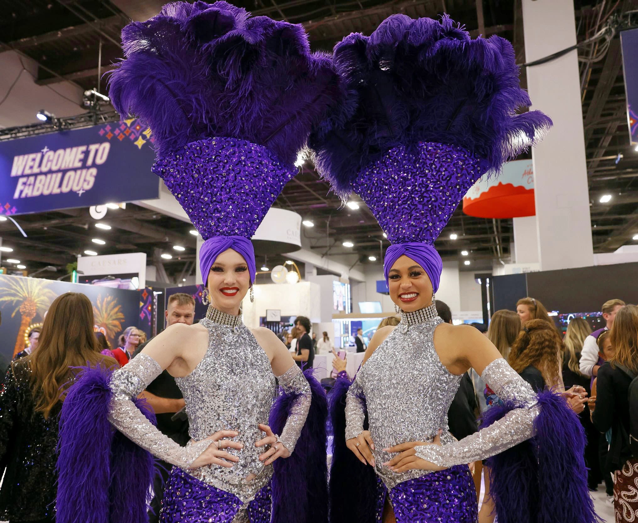Two females in glittery outfits and feathered headpieces smiling at the camera