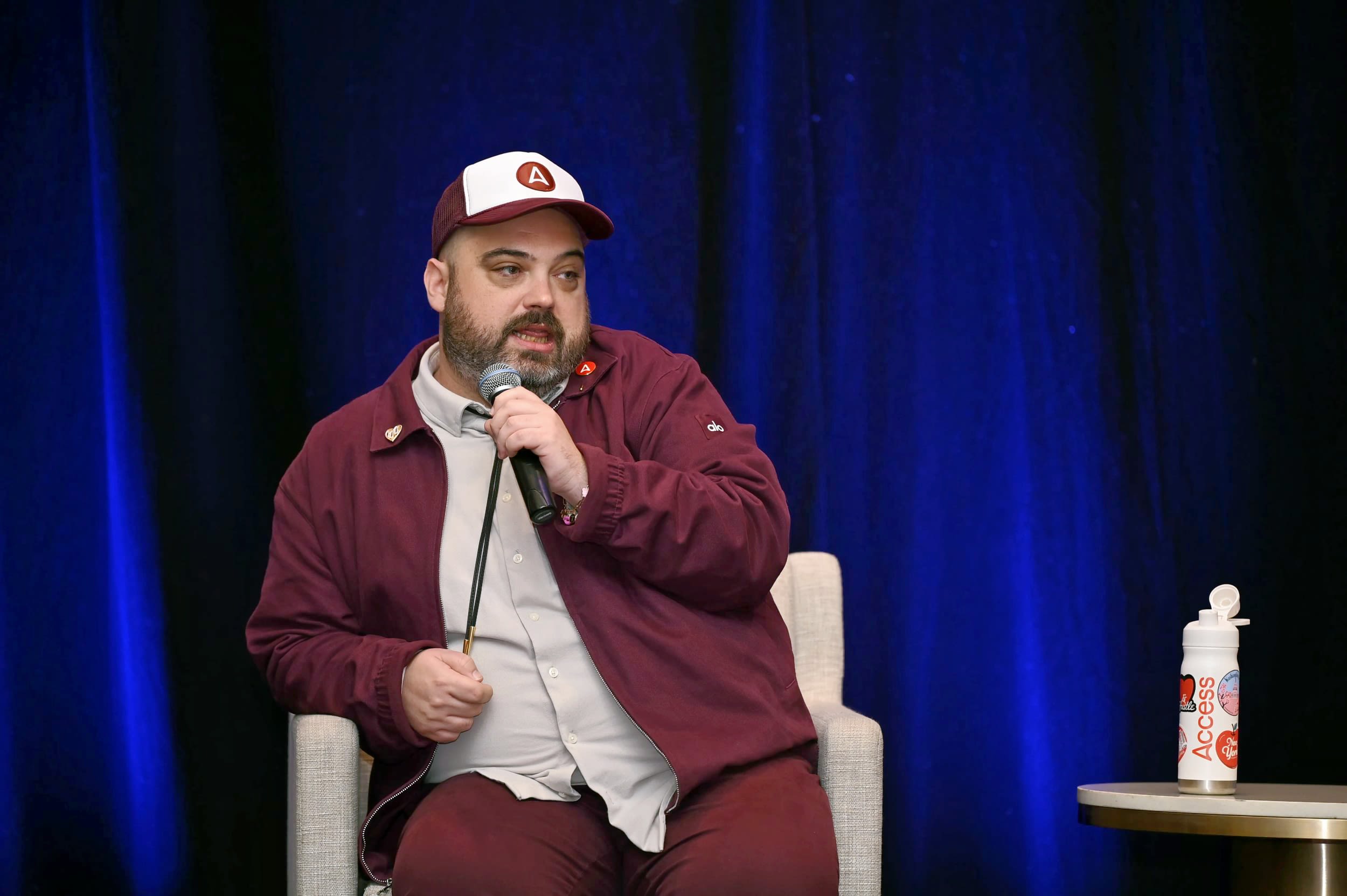 Male in a baseball cap onstage with a mic at the future leaders forum 